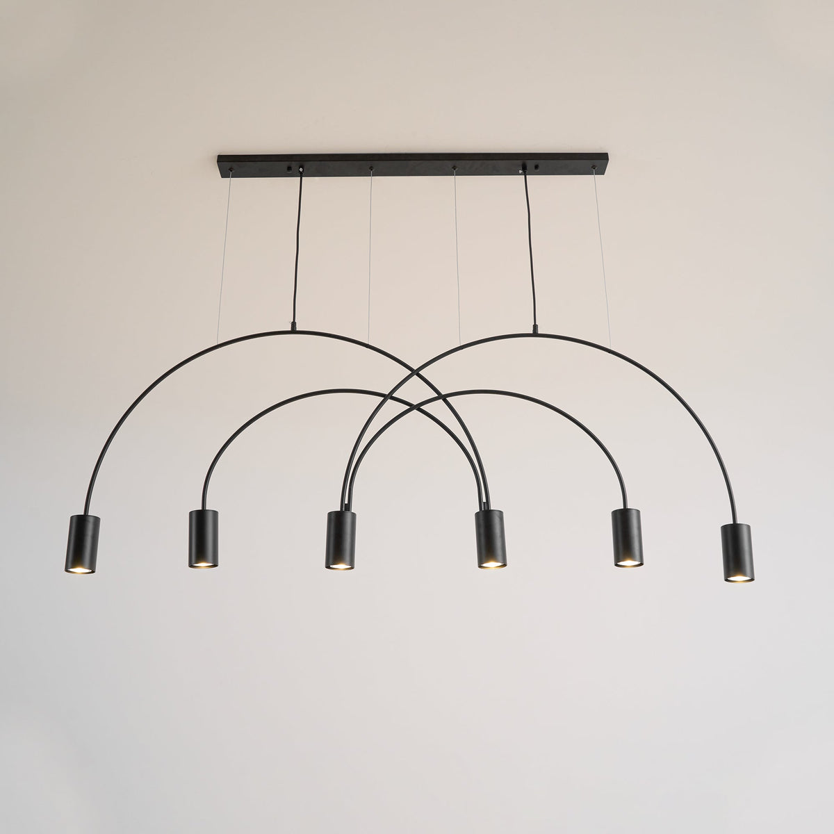 Front view of this Clérachic arch pendant in black, six spot heads below a slim canopy bar on a pale wall.