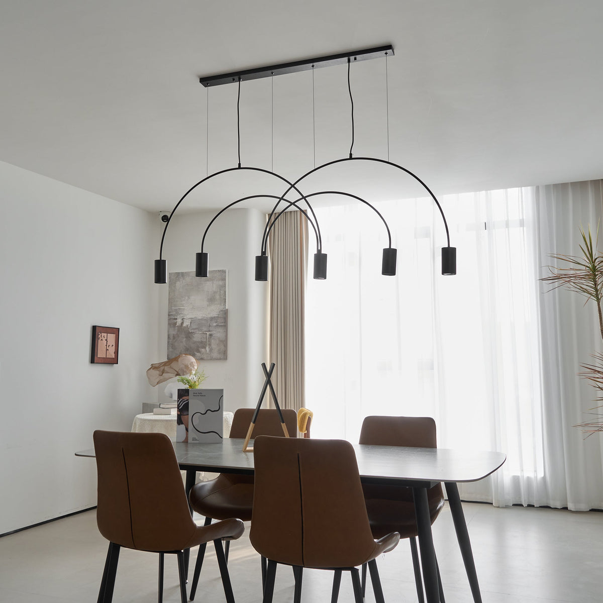In a white dining room with floor-length curtains, this black Clérachic arch pendant hangs above a slate-topped table and brown chairs.