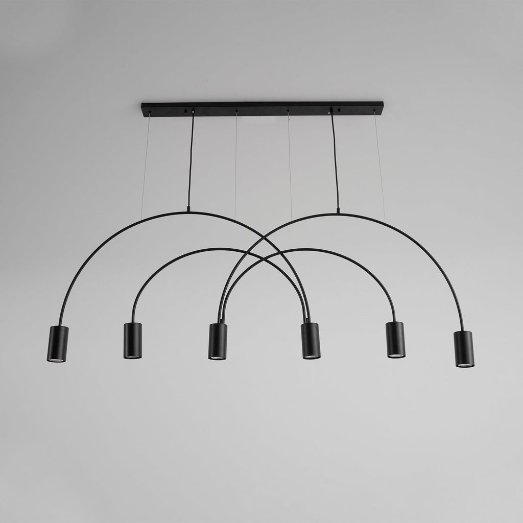 Black Clérachic arch pendant against a plain grey wall, its six spot heads hanging at staggered heights below the canopy bar.