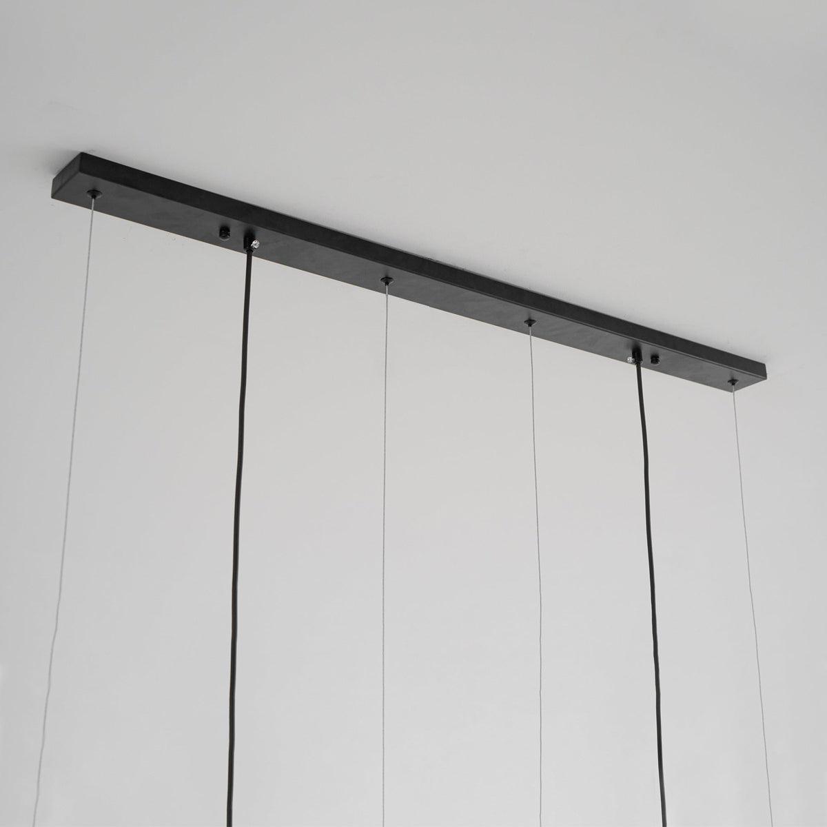 Underside of the slim black canopy bar on this Clérachic pendant, with fine suspension wires and two thicker power cords.