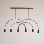 Black Clérachic arch pendant with six spot heads and a flat canopy bar, shown on a warm off-white wall.