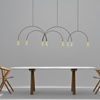 Eight small brass spot heads hang from thin black arches on this Clérachic pendant, above a long white table with walnut legs.