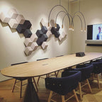 This Clérachic arch pendant hangs in a meeting room with a pale oval wooden table, navy chairs and a hexagon tile wall.
