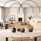 Brass spot heads on black arches, this Clérachic pendant hangs over a round stone table in a pale living room.