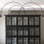 Black Clérachic arch pendant, its spot heads glowing, hung in front of a tall black glazed cabinet.