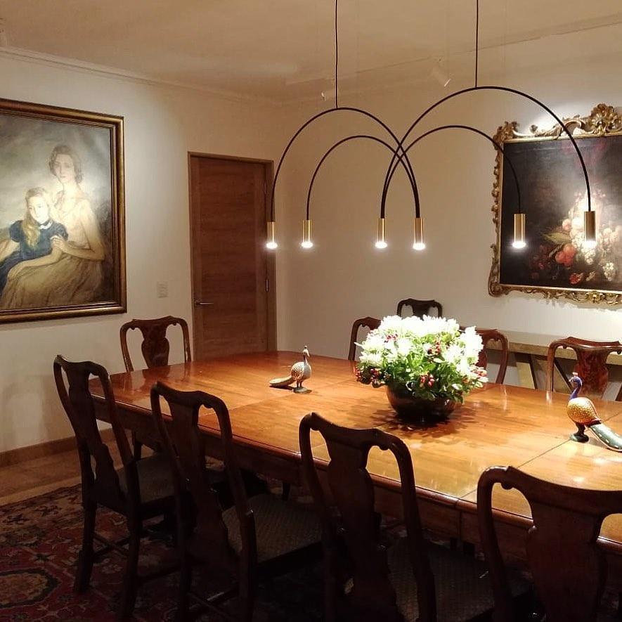 This Clérachic arch pendant hangs over a long polished dining table, with gilt-framed portraits on the walls behind it.