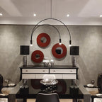 Lit spot heads on a black Clérachic arch pendant, above a white and black sideboard with three red round mirrors behind.