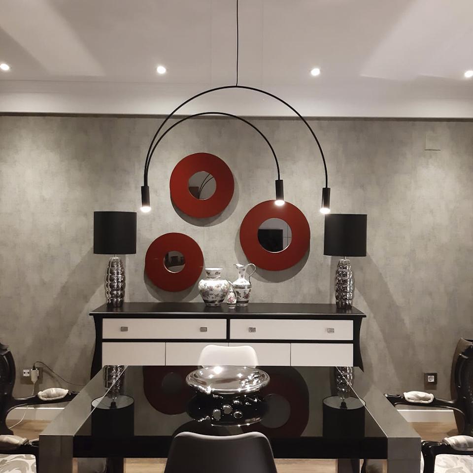 Lit spot heads on a black Clérachic arch pendant, above a white and black sideboard with three red round mirrors behind.