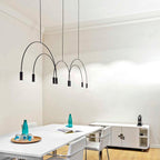 Black Clérachic arch pendant in a white room with cornice mouldings, above a table set with teal glass bottles.
