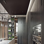 Seen at the edge of a dark kitchen, this Clérachic arch pendant hangs near a wine rack and built-in ovens.
