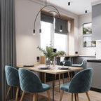 A black Clérachic arch pendant lit by a window, above a wooden dining table with teal velvet chairs.
