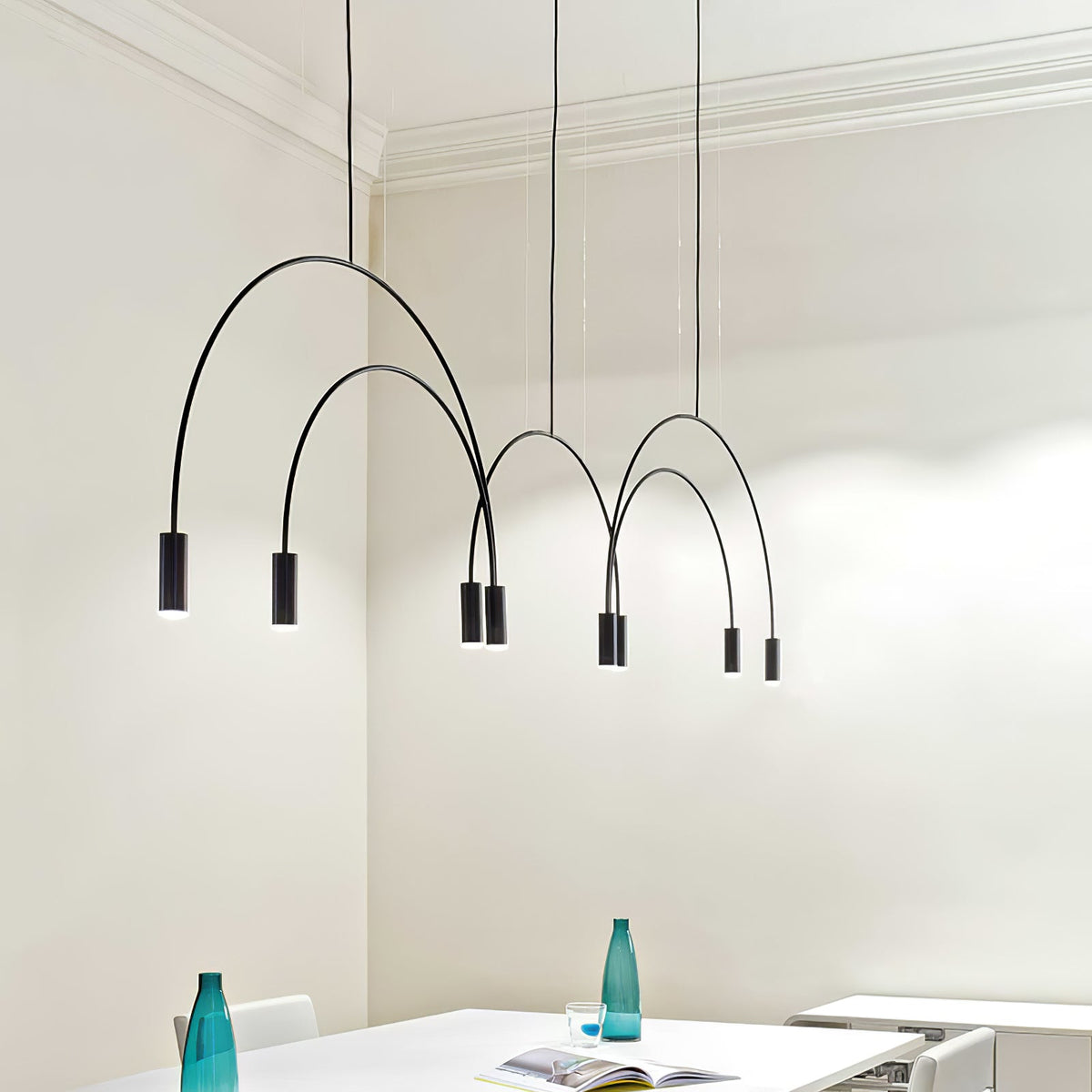 Black Clérachic arches and spot heads hang at different heights in a cream room with cornices, above a white table.