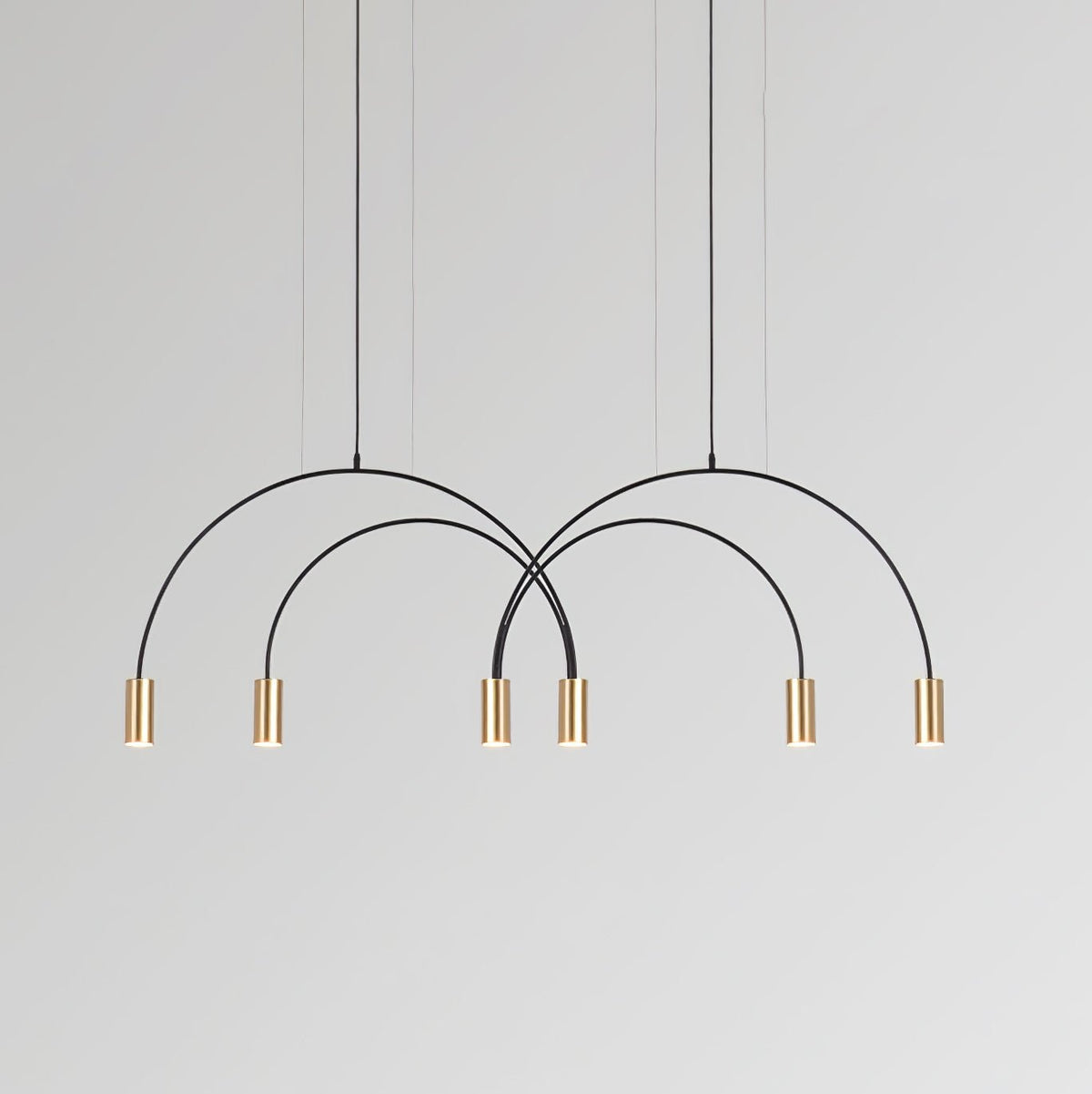Six brass spot heads under two crossing black arches, this Clérachic pendant on a soft grey backdrop.