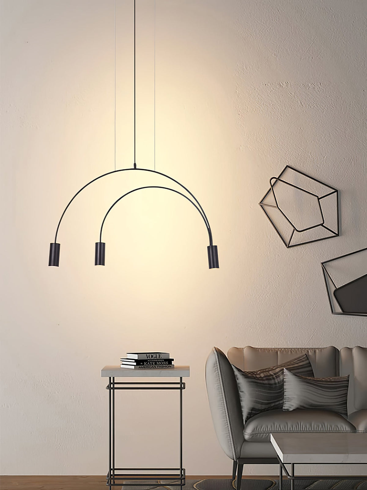 Three black spot heads under two curved arches, this Clérachic pendant glows beside a grey sofa and a wire side table.