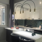 Brass spot heads on tall black arches, this Clérachic pendant hangs in a white kitchen with a green geometric splashback.