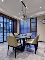 High view of a Clérachic arch pendant over a dark dining table, with cream chairs and black-framed windows behind.