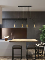 Four brass spot heads under shallow black arches, this Clérachic pendant hangs in a dark kitchen with high stools.