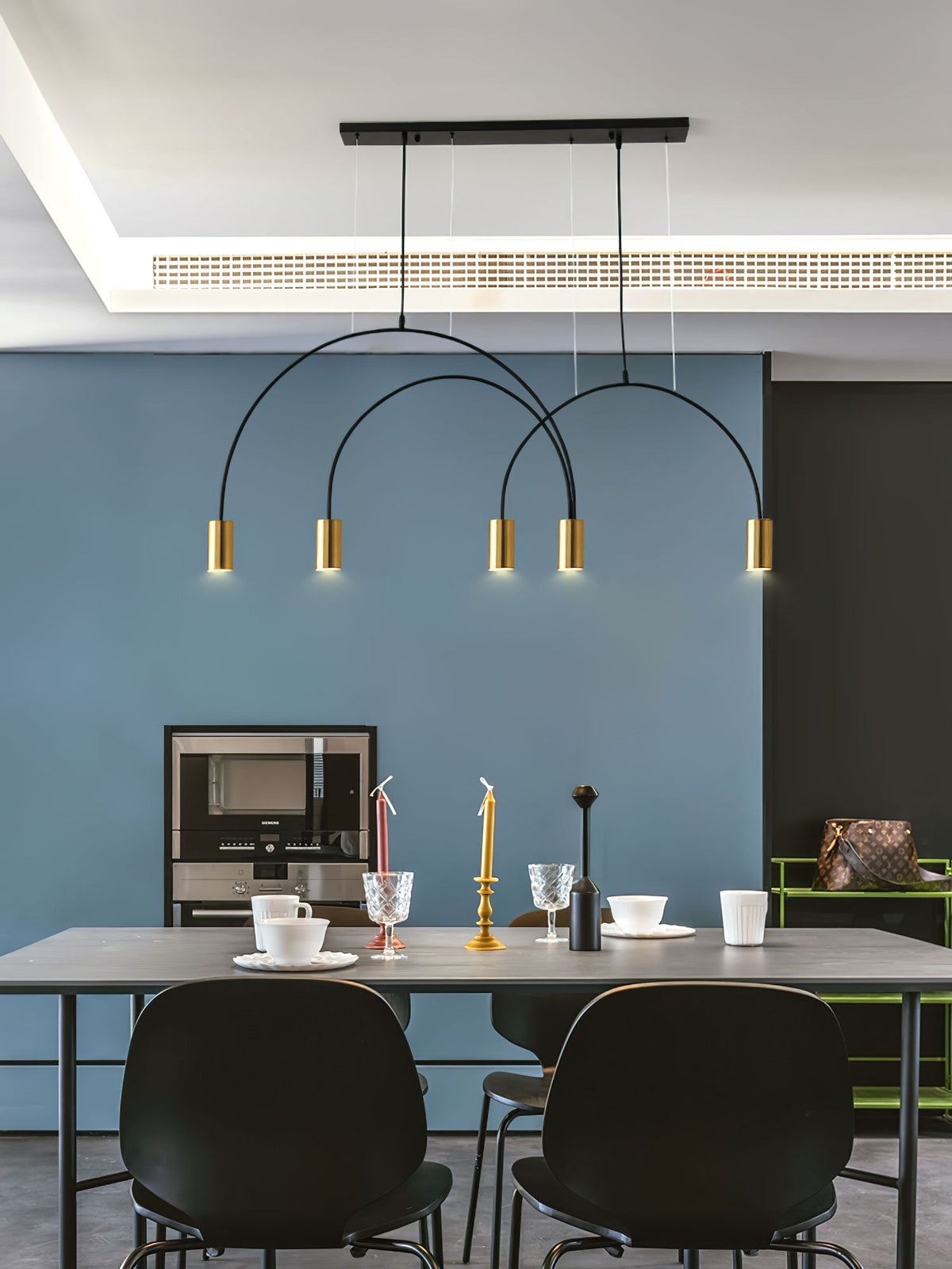 Brass spot heads and a black canopy bar, this Clérachic pendant hangs above a grey table against a blue wall.