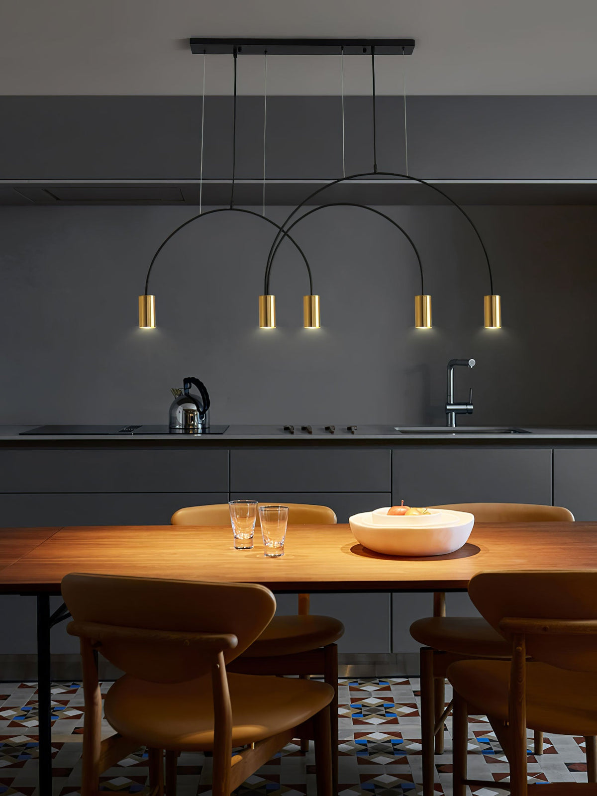 Four brass spot heads hang below a black canopy bar on this Clérachic pendant, over a wooden table in a dark kitchen.