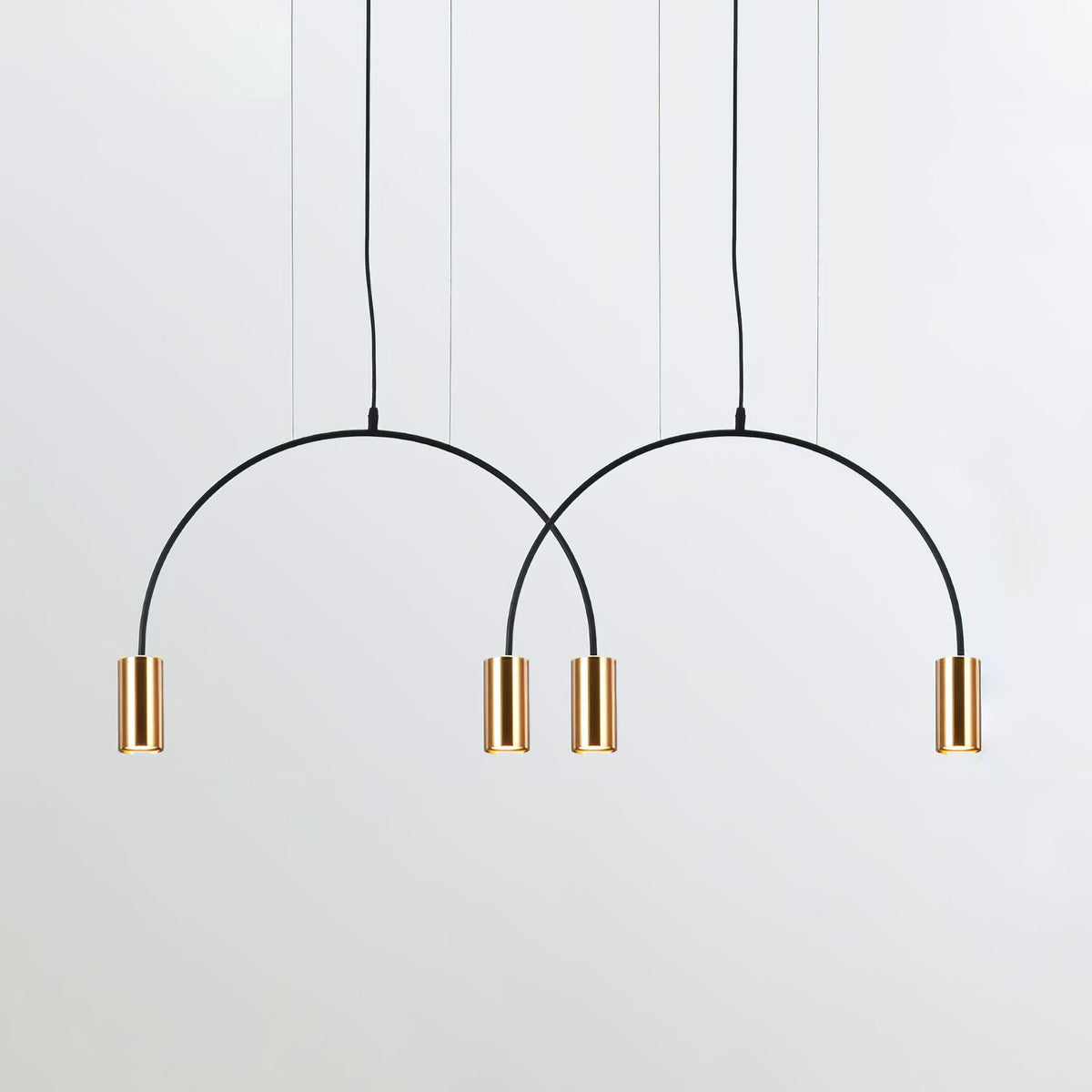Two black arches and four brass spot heads, this Clérachic pendant seen against a pale backdrop.