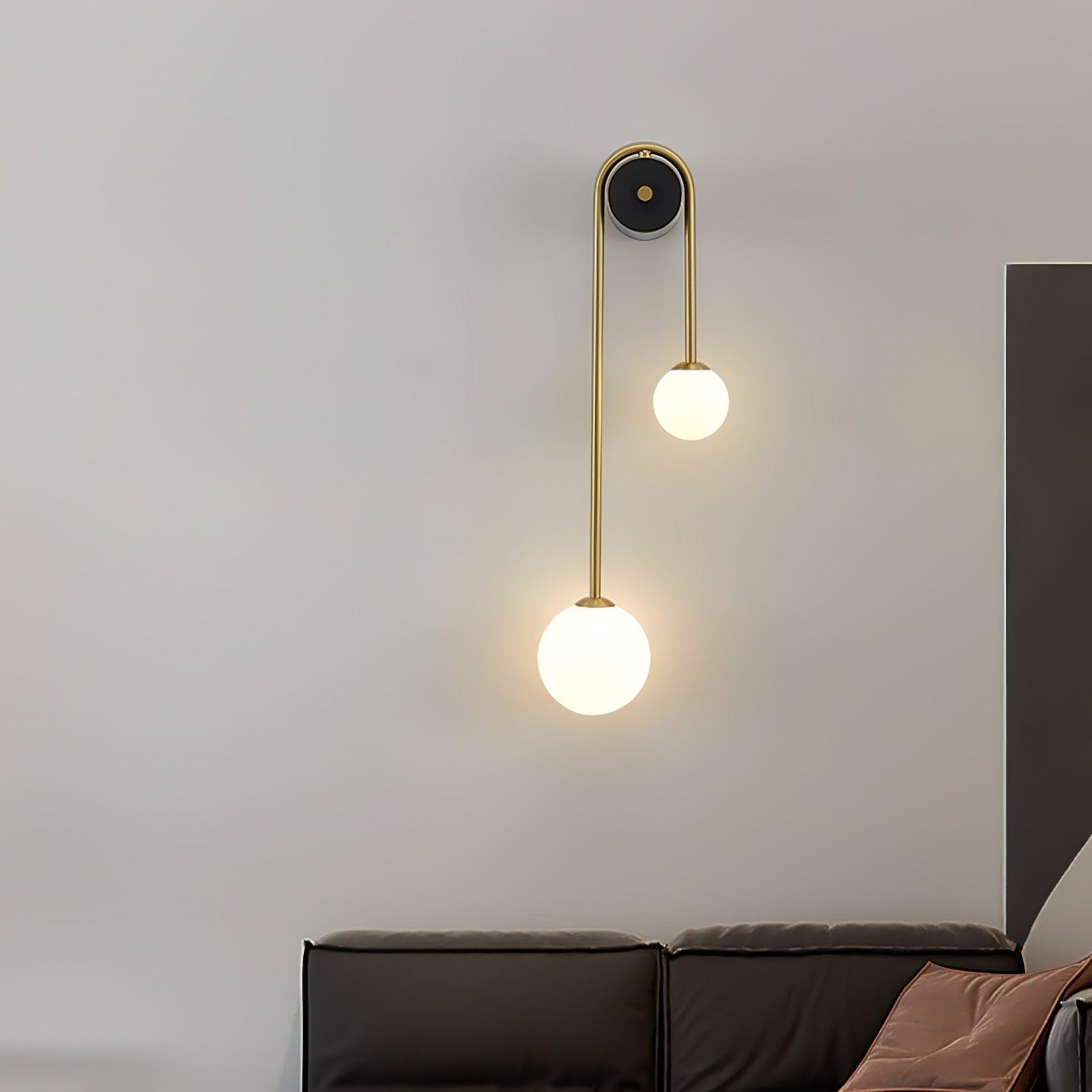 Clérachic arched brass sconce above a dark leather sofa, both frosted globes casting a warm pool up the grey wall.