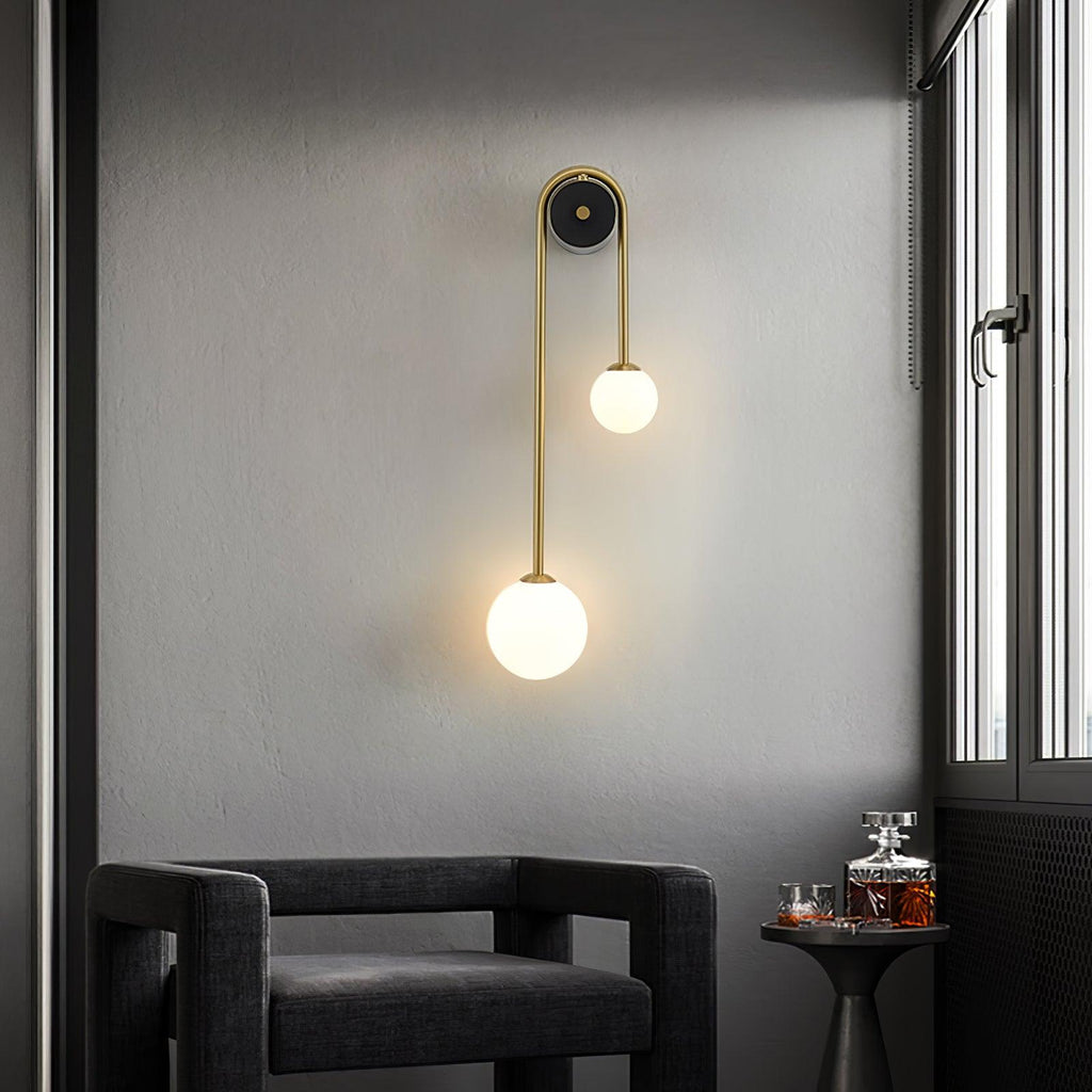 Clérachic arched brass wall sconce beside a window in a grey corner, lighting an armchair and a small drinks table.