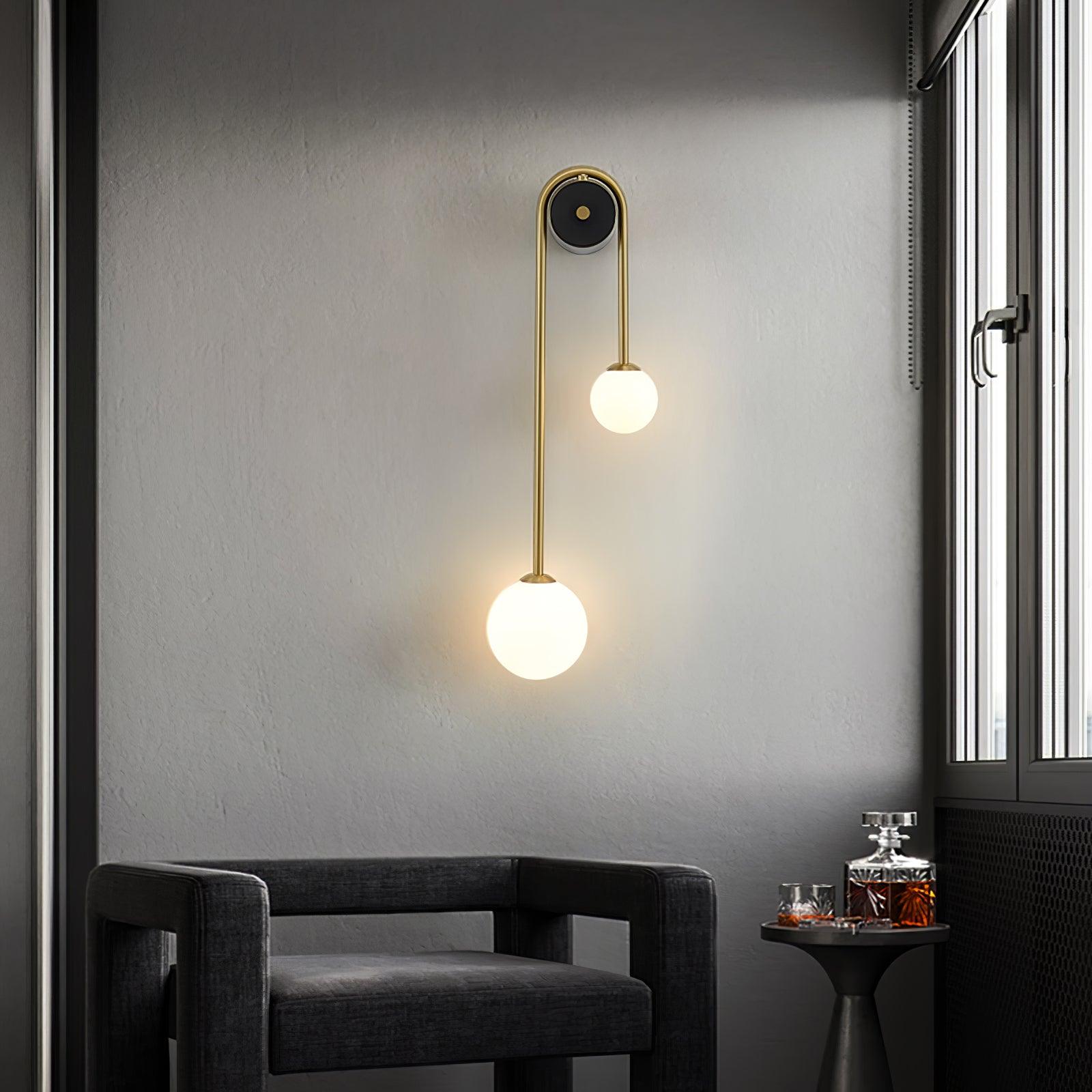 Clérachic arched brass wall sconce beside a window in a grey corner, lighting an armchair and a small drinks table.