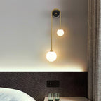Clérachic arched brass sconce at a bedside, the lower globe level with a dark woven headboard and two green glasses.