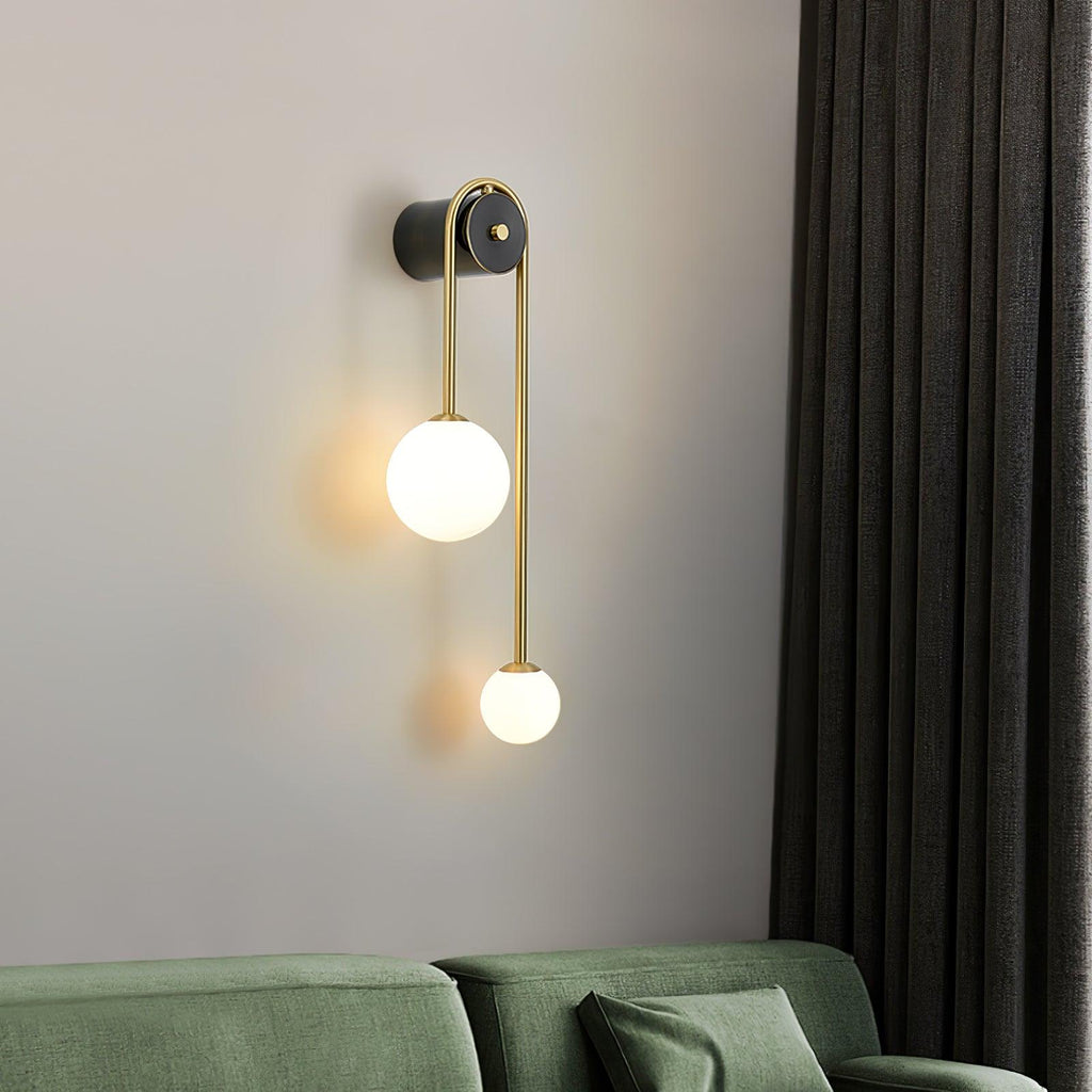 Clérachic arched brass wall sconce over a green sofa, the larger globe held high and the small one dropping below.