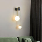 Clérachic arched brass wall sconce over a green sofa, the larger globe held high and the small one dropping below.