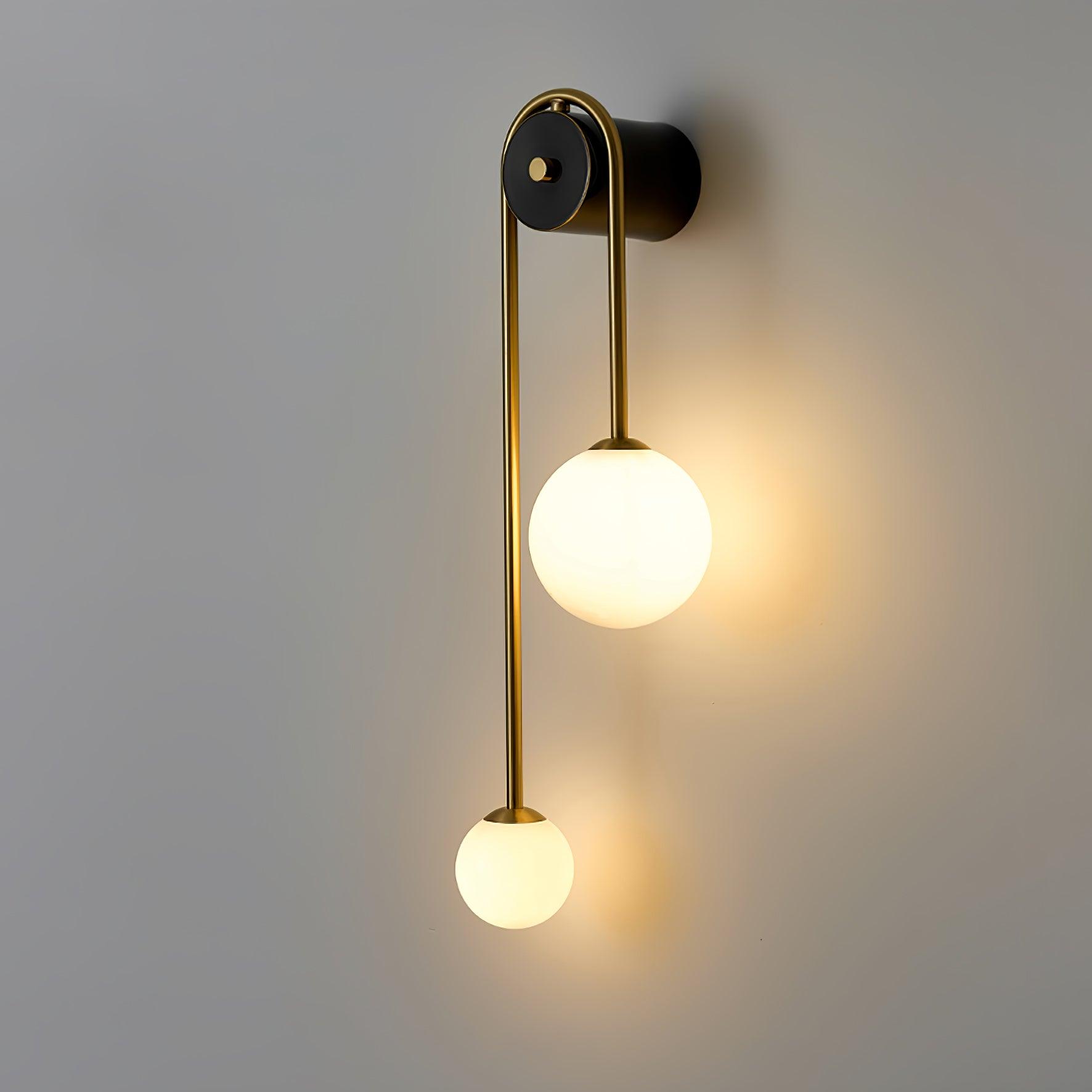 Angled view of the Clérachic arched brass wall sconce, warm light pooling on the grey wall behind the lit globes.