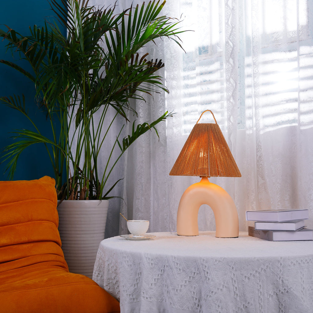 Skin arched Clérachic lamp on a small round table in a corner with an orange armchair, a tall palm and white curtains.