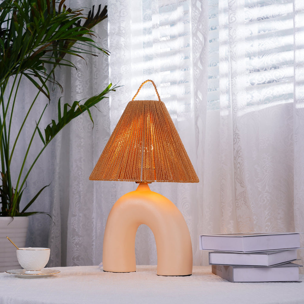 Skin ceramic arch base and rope-wrapped shade of this Clérachic lamp, lit beside a teacup and books by sheer curtains.