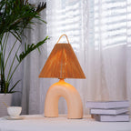 Skin ceramic arch base and rope-wrapped shade of this Clérachic lamp, lit beside a teacup and books by sheer curtains.