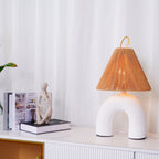 Wide view of a white arched Clérachic lamp on a white sideboard with gold handles, with a figurine and stacked books.