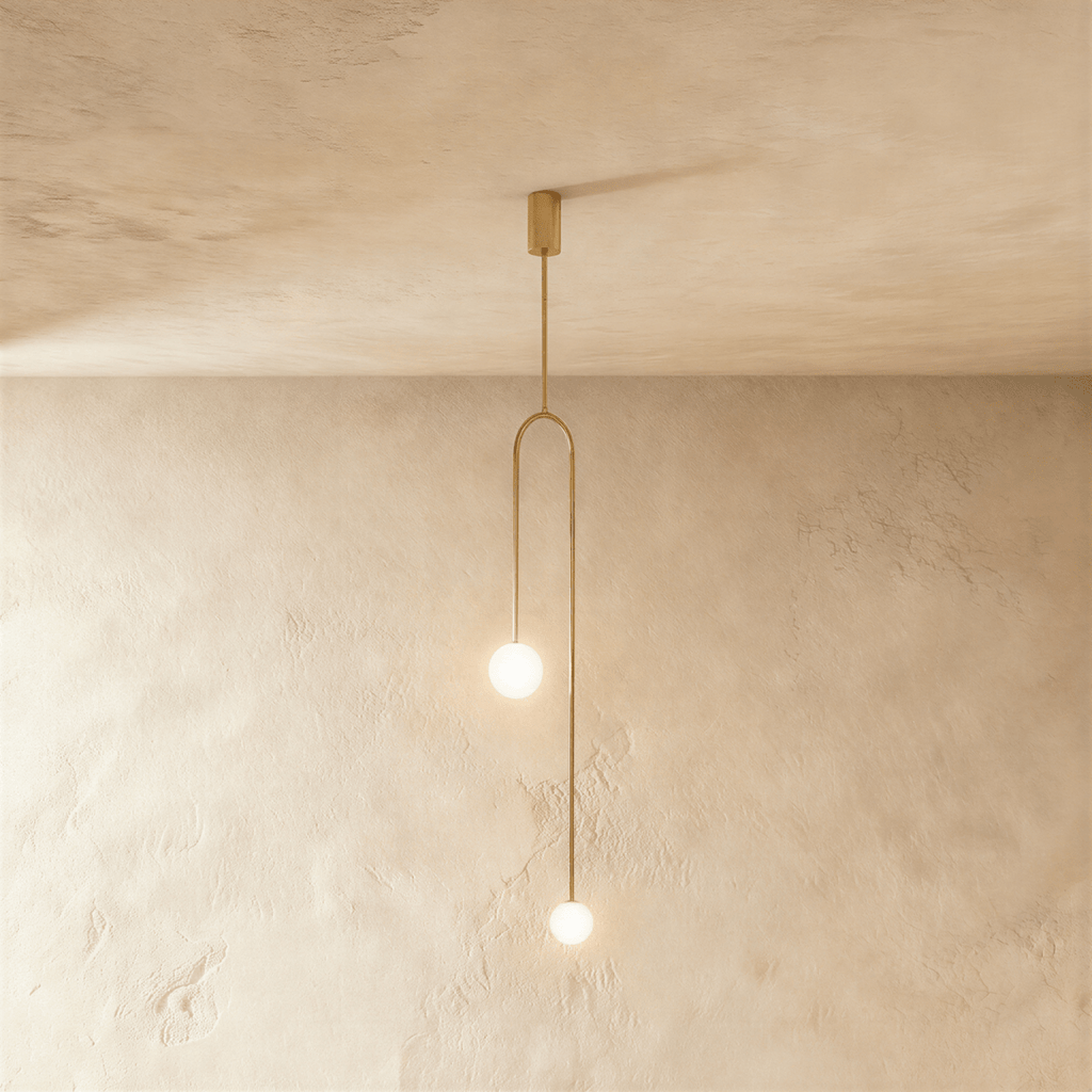 Clérachic slim arch pendant in gold with two glowing frosted globes at different heights, against limewashed plaster.
