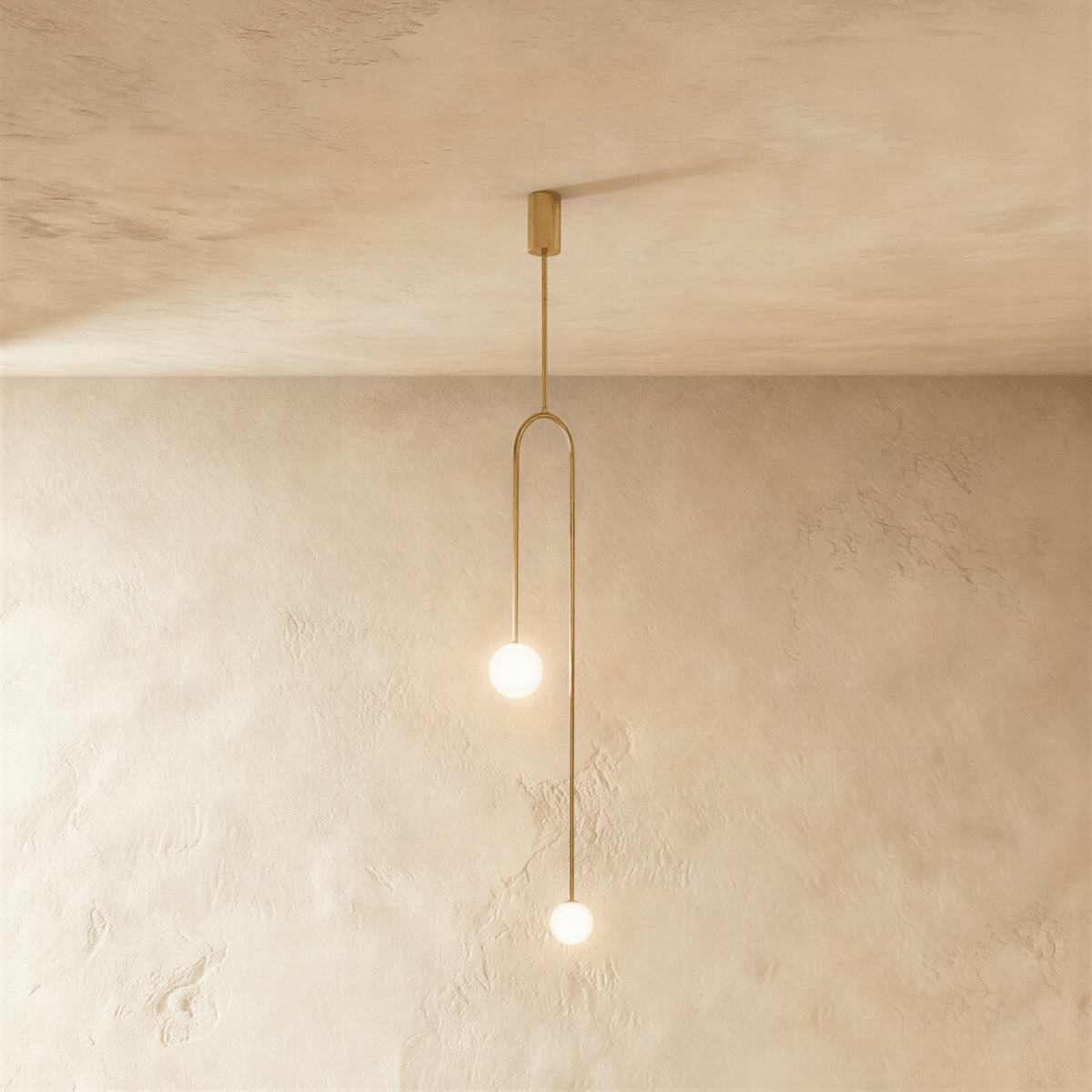 Clérachic slim arch pendant in gold with two glowing frosted globes at different heights, against limewashed plaster.