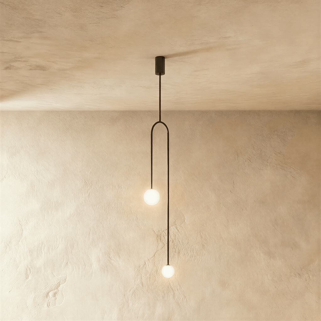 Clérachic slim black arch pendant with two glowing frosted globes at different heights, against limewashed plaster.