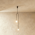 Clérachic slim black arch pendant with two glowing frosted globes at different heights, against limewashed plaster.