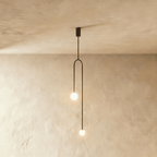 Clérachic slim black arch pendant with two glowing frosted globes at different heights, against limewashed plaster.