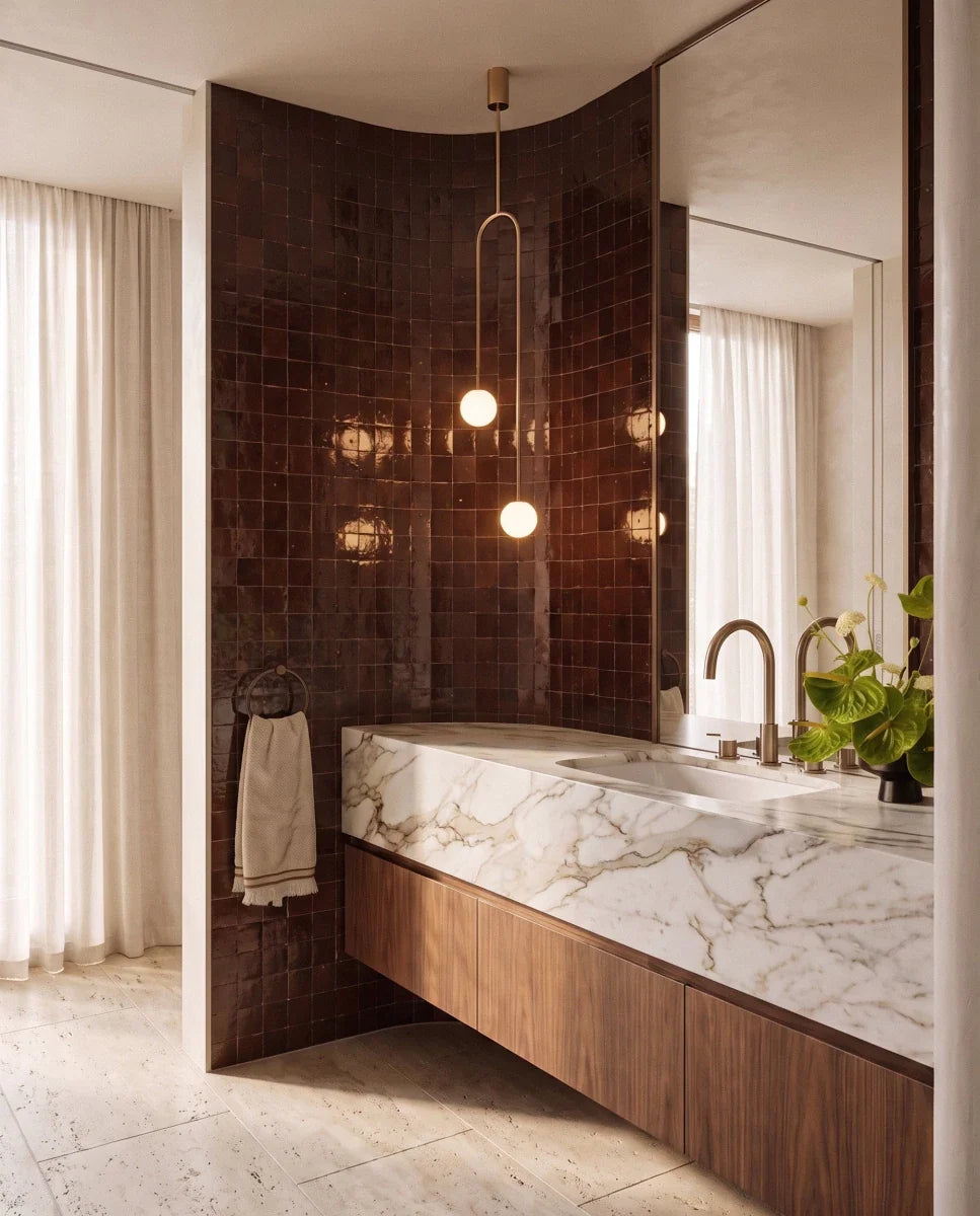 Clérachic gold arch pendant with two lit globes hanging by a curved glazed tile wall, beside a mirror above a wooden vanity.