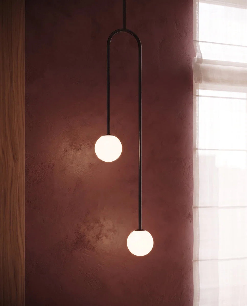 Close view of the Clérachic black arch pendant, two frosted globes glowing warm against a plum plaster wall.