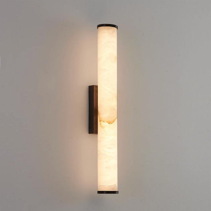 Clérachic alabaster sconce with a bronze-black bracket, the veined stone column lit warm on pale grey plaster.
