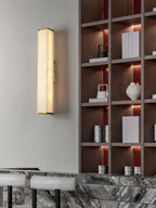 The Clérachic brass sconce mounted beside dark timber shelving, its warm glow set against a veined marble counter.