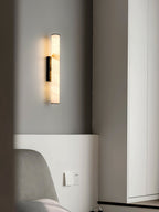 Clérachic sconce with a black bracket lighting a bedroom corner beside an upholstered chair and full-height mirror.