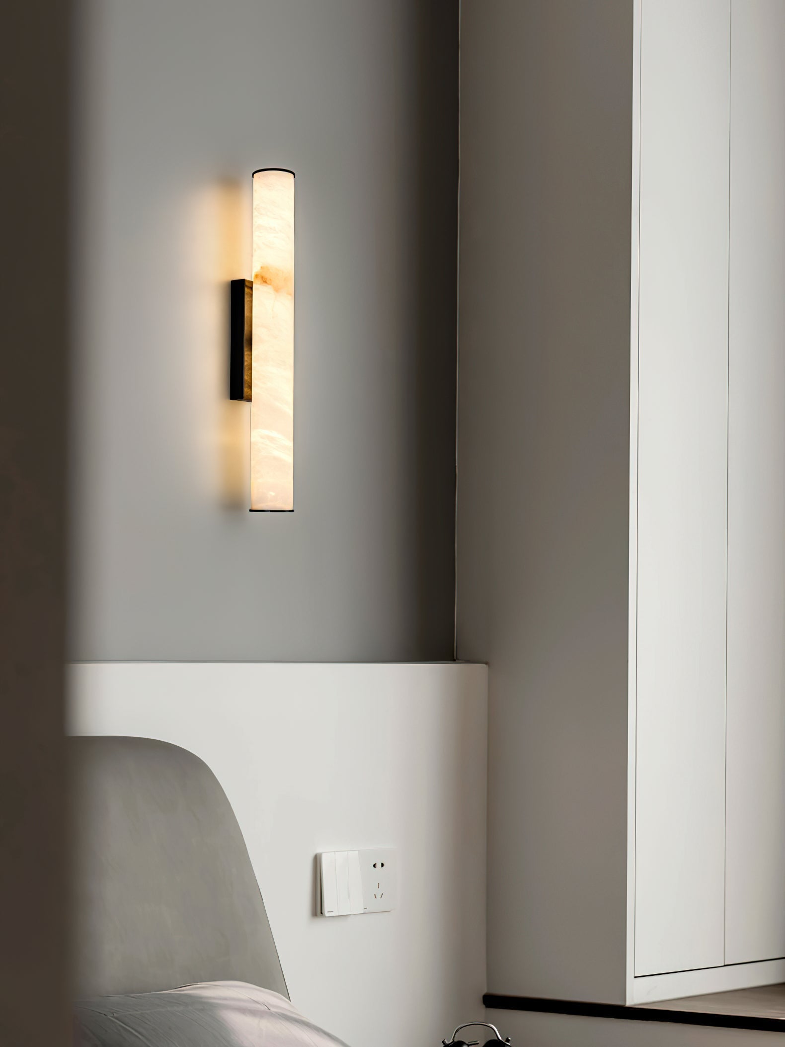 Clérachic sconce with a black bracket lighting a bedroom corner beside an upholstered chair and full-height mirror.