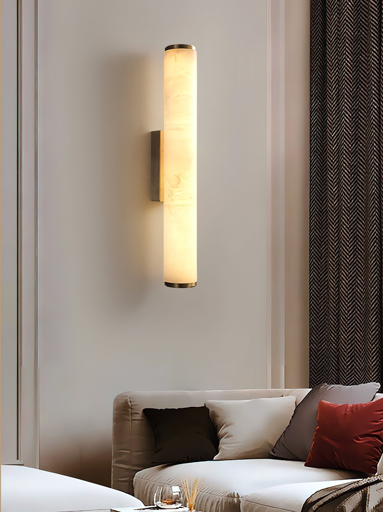 Clérachic alabaster sconce on a panelled wall, warming a living room with herringbone drapery and a red cushion.
