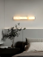 Clérachic sconce mounted horizontally above a bed, its long alabaster bar washing the headboard wall in warm light.