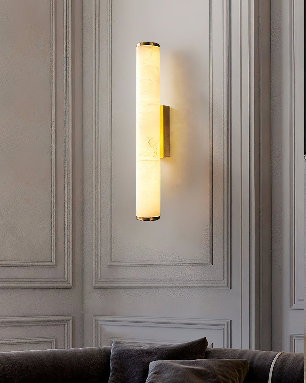 The Clérachic sconce on classic moulded panelling, its alabaster column lit above a low charcoal sofa.