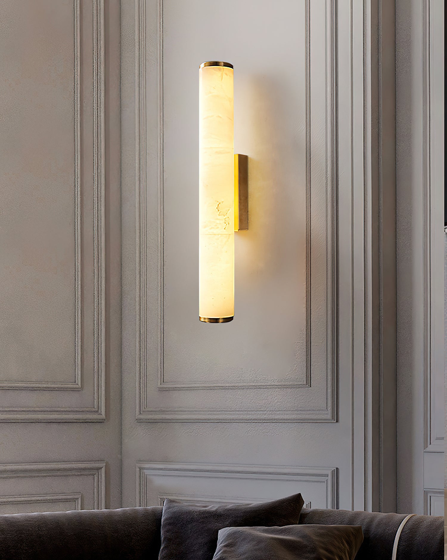 The Clérachic sconce on classic moulded panelling, its alabaster column lit above a low charcoal sofa.